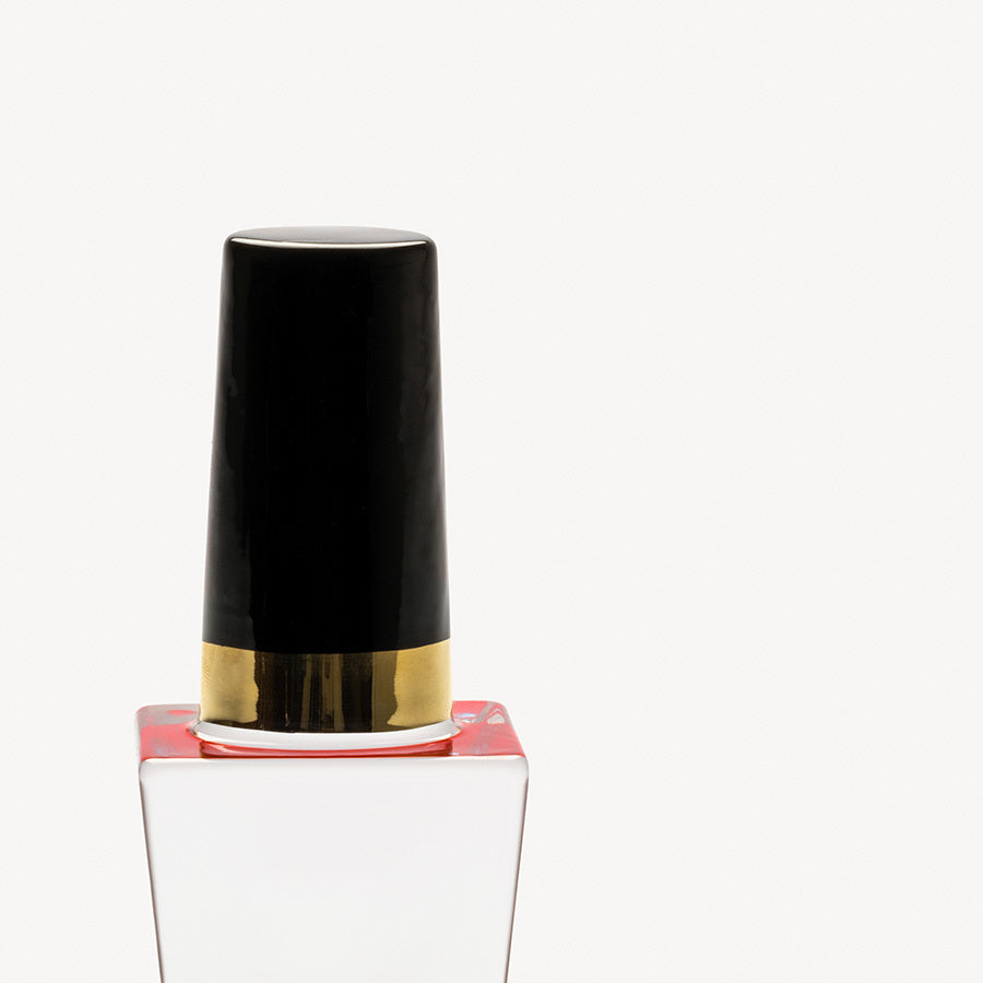 A close-up of the KostaBoda: Nail Polish Poppy Red bottle with a black and gold cap on a white background exudes elegance akin to Åsa Jungneliuss innovative designs for Kosta Boda.