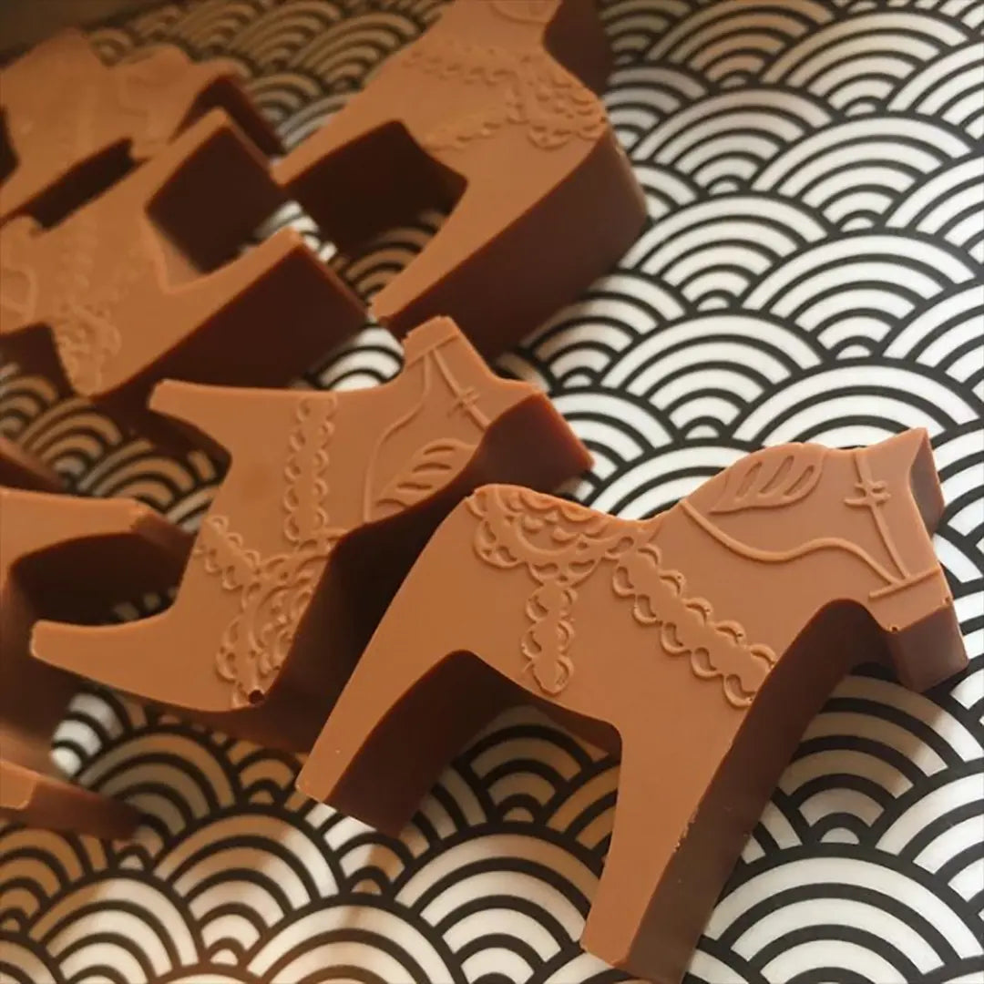 Chocolate pieces shaped like Dala Horses are placed on a black and white patterned tray, crafted using the Candy Mold: Dalahast Pralinform.