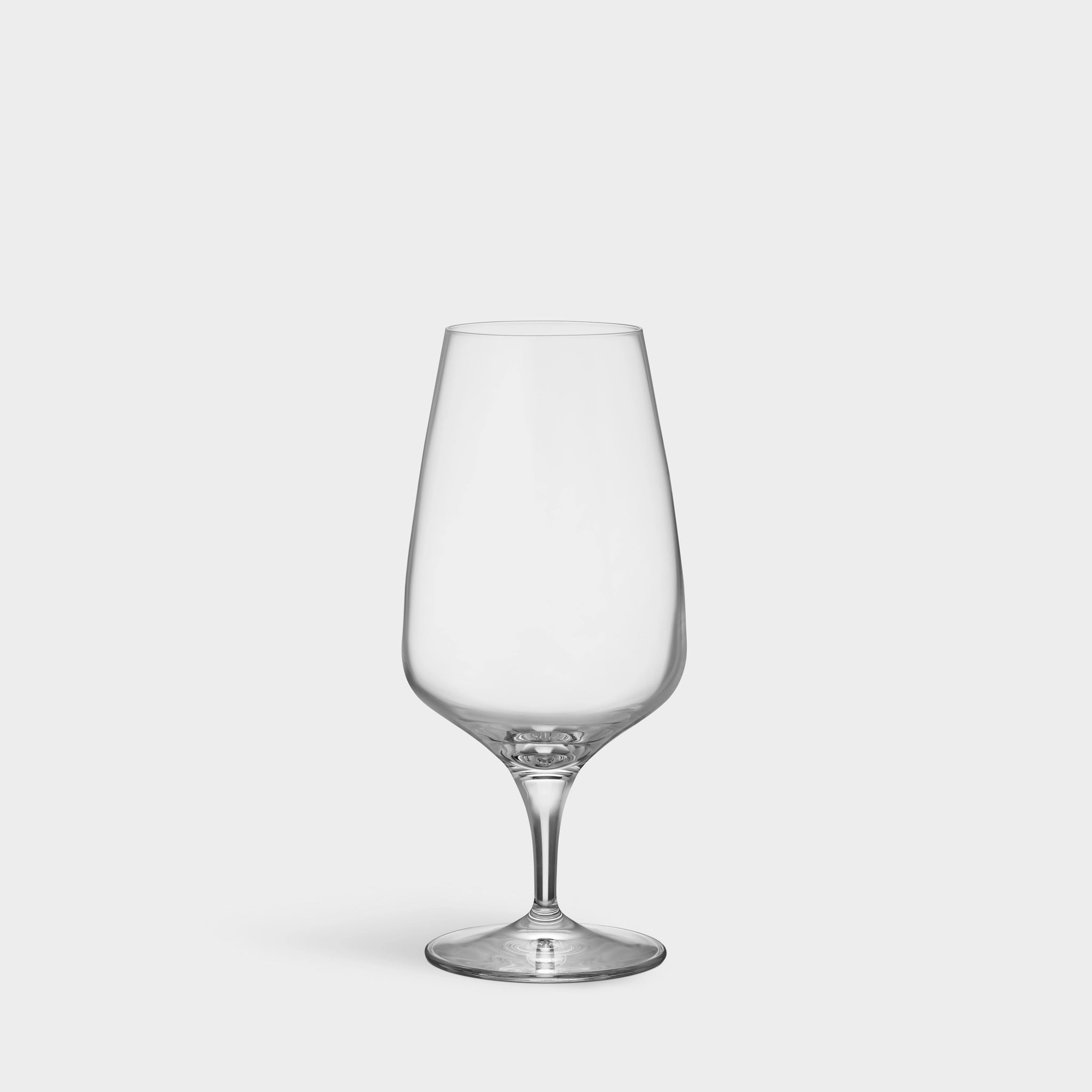 A clear, empty Orrefors Pulse beer glass with a short stem and round base exudes Scandinavian simplicity against a plain light gray background.