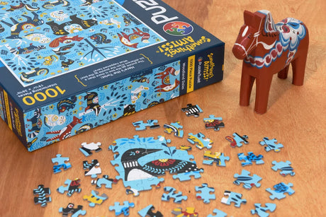 Partially assembled puzzle with a blue bird design on a wooden table, next to its box and a red Swedish Dala horse figurine.