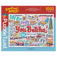 1000-piece puzzle box with Minnesota slang such as “You Betcha!” shown in playful fonts, surrounded by cartoon doodles and bright accents on a white background.