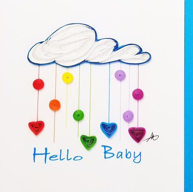 The "Cards: Hello Baby Raining Cloud Quilling Card 4x4" beautifully captures a hand-crafted, white quilled paper cloud mobile surrounded by vibrant hearts and circles, evoking the image of a raining cloud. Below this delightful scene, the elegant text "Hello Baby" is inscribed in blue.