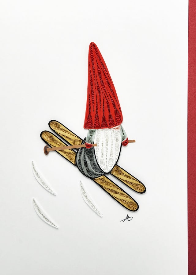 The "Skiing Gnome God Jul Quilling Card" is a charming piece of quilled paper art showcasing a gnome in a red hat, white beard, and yellow skis. Ideal for bringing holiday cheer, this delightful card features a cheerful "God Jul" message.