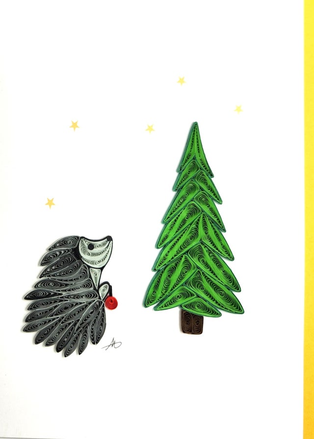 The Card: Hedgehog with Christmas Tree Quilling Card 5x7 features a quilled paper hedgehog holding a red ornament beside a Christmas tree with yellow stars—an ideal choice for a festive handmade holiday greeting.