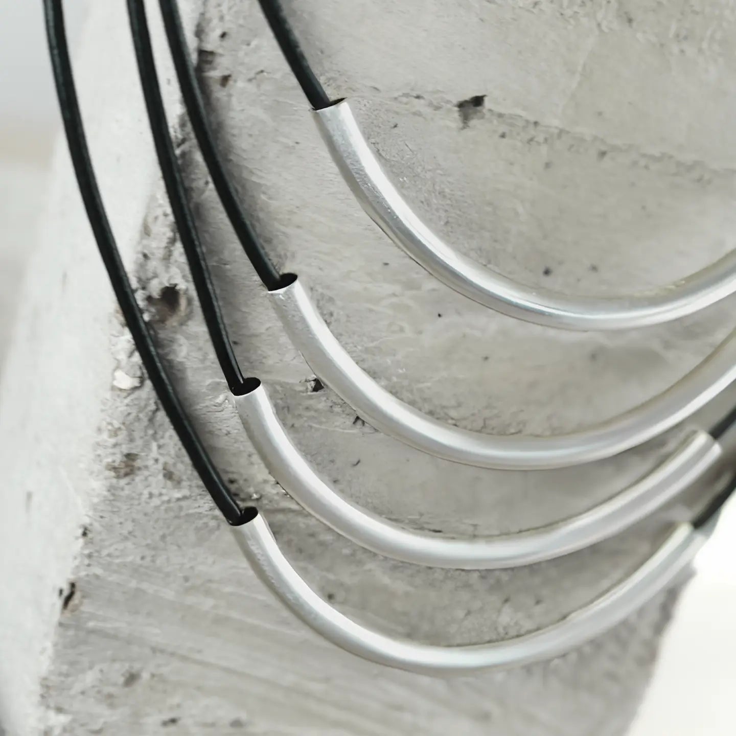 Four Necklace: Short Multi String Leather Necklace Silver Plating pieces with silver-curved metal pendants are draped against a textured, gray concrete surface.