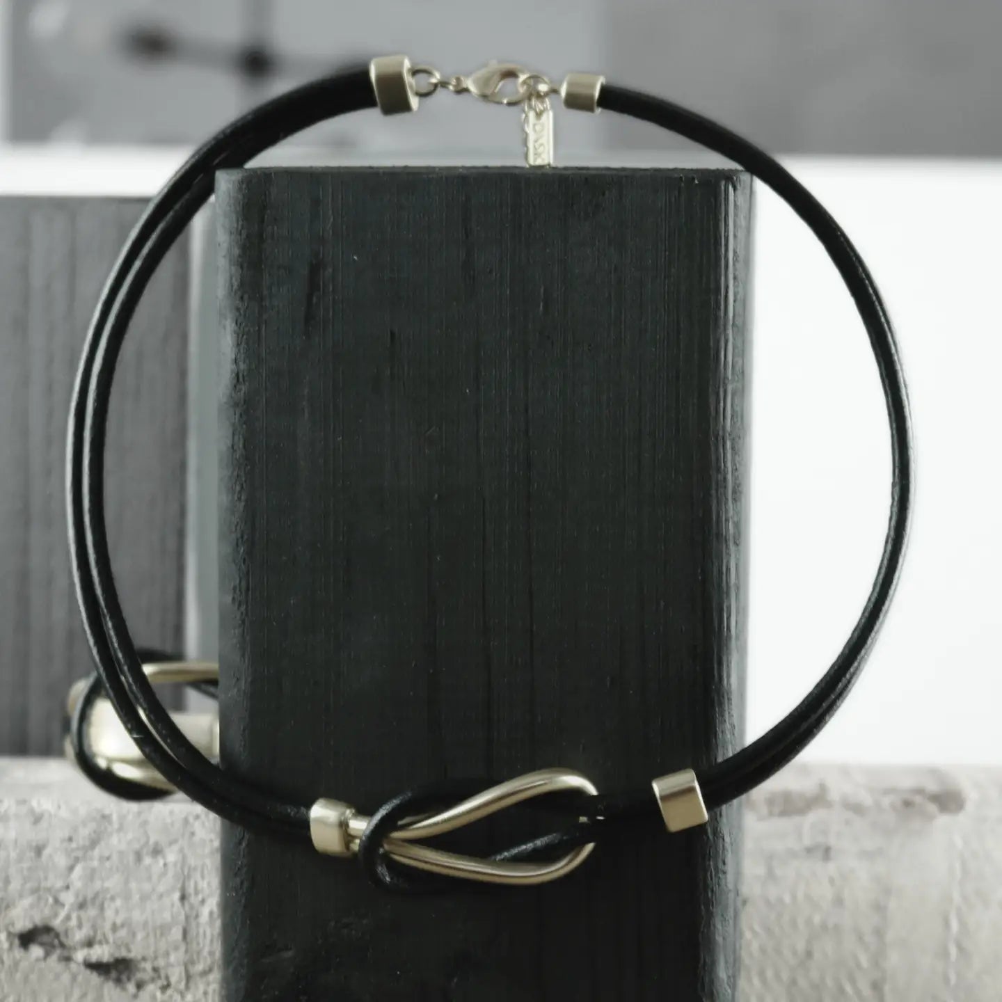 A Short Togetherness leather necklace featuring gold plating is elegantly draped around a sleek black rectangular stand.