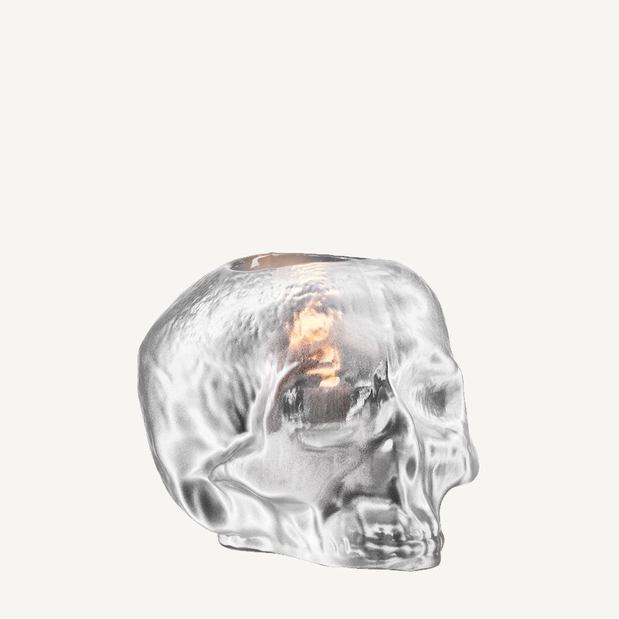 KostaBodas Still Life Votive Candle Holder features a glass skull with a reflective surface and an orange glow inside, reminiscent of a silver votive, set against a plain background.