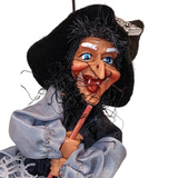 A close-up of the Figurine: Kitchen Witch Doll – Sirene Silver (10.2" Tall) with a large nose, blue eyes, black hat, and gray clothing, holding a broomstick for good luck as inspired by Northern European folklore.