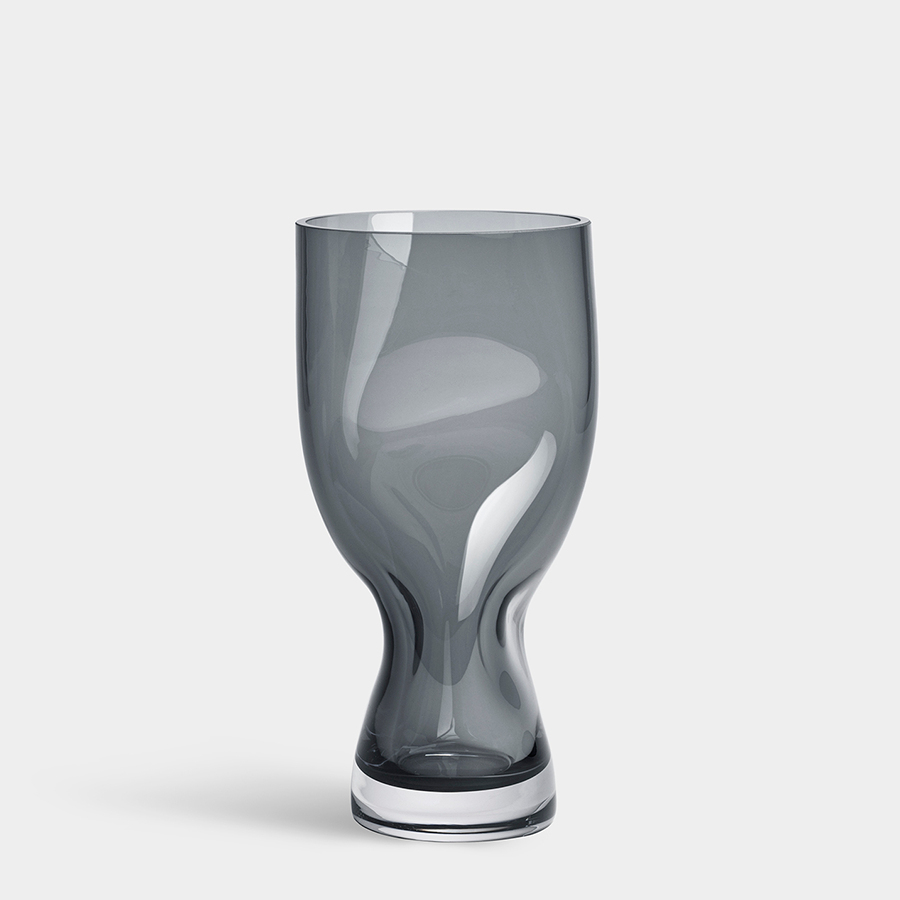 A gray, uniquely shaped glass vase with a rounded, irregular base stands on a plain white background, reflecting the elegant design of Orrefors Squeeze Blue/Gray Vase Small by Lena Bergström.