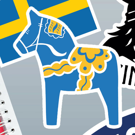 Blue Swedish Dala Horse sticker with yellow patterns in front of a Swedish flag sticker, both on a gray background.