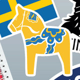 Yellow and blue Swedish Dala horse sticker on grey background with a Swedish flag behind it; edges of additional partial stickers are visible nearby.