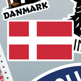 Rectangular Danish flag sticker with a white Scandinavian cross on a red background, shown among other Nordic stickers and the edge of a spiral notebook.