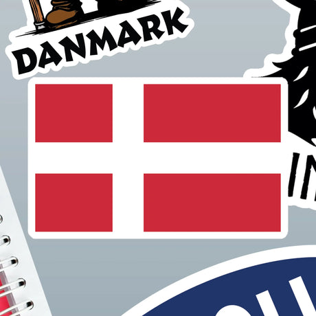 Rectangular Danish flag sticker with a white Scandinavian cross on a red background, shown among other Nordic stickers and the edge of a spiral notebook.