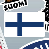 Finnish flag sticker featuring a blue Nordic cross on a white background, shown next to other stickers and the edge of a spiral notebook.