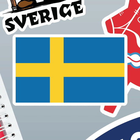 Sticker with a yellow Nordic cross on a blue background, representing Sweden, shown among other partially visible stickers and miscellaneous objects.