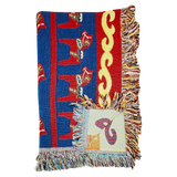 Woven blanket with red, blue, and yellow patterns, Swedish Dala horse designs, multicolored fringes, and a visible square patch.