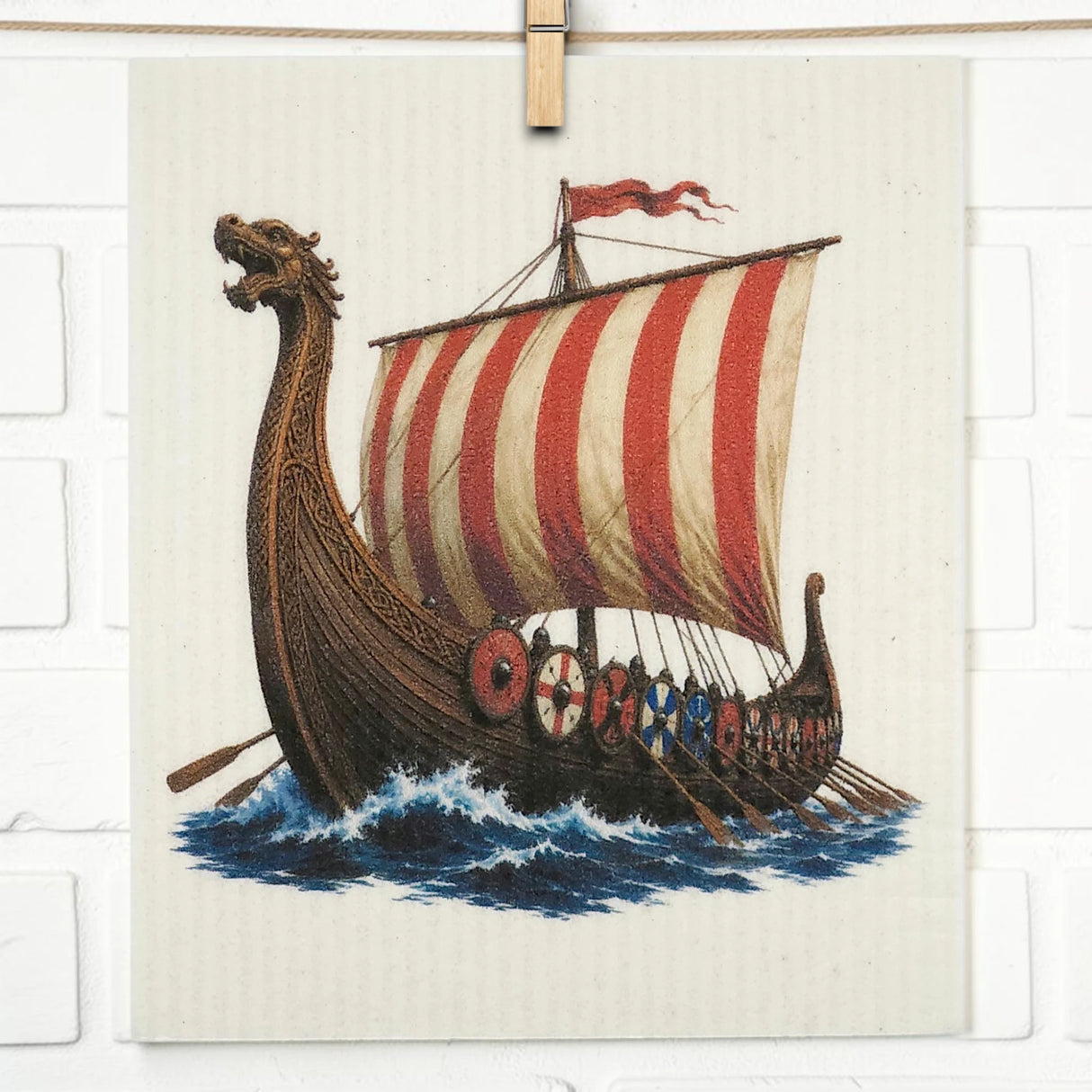 Kitchen cloth with a Viking longship design, showing a dragon-headed prow, striped sail, rows of shields and oars, sailing on stylized blue waves.