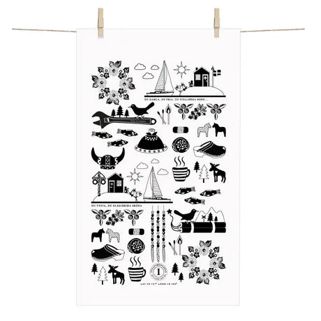 The Made in Sweden Terry-Cotton Towel by Anneko Design Sweden, featuring black Scandinavian-style illustrations on white cotton, including birds, trees, houses, and the iconic Dala horse, hangs on a clothesline with wooden clothespins.