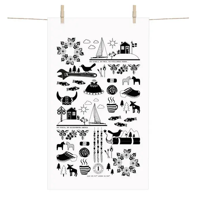 The Terry Towel, made in Sweden, features Nordic-style black and white designs with Swedish symbols, animals, trees, flowers, and boats. Crafted from soft cotton, it hangs elegantly on a clothesline with wooden pegs.