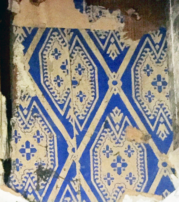 A section of torn vintage wallpaper with a blue and beige geometric and floral pattern reminiscent of Kerstin Landströms Blaklint Cornflower blanket, made from 100% Norwegian lambs wool.