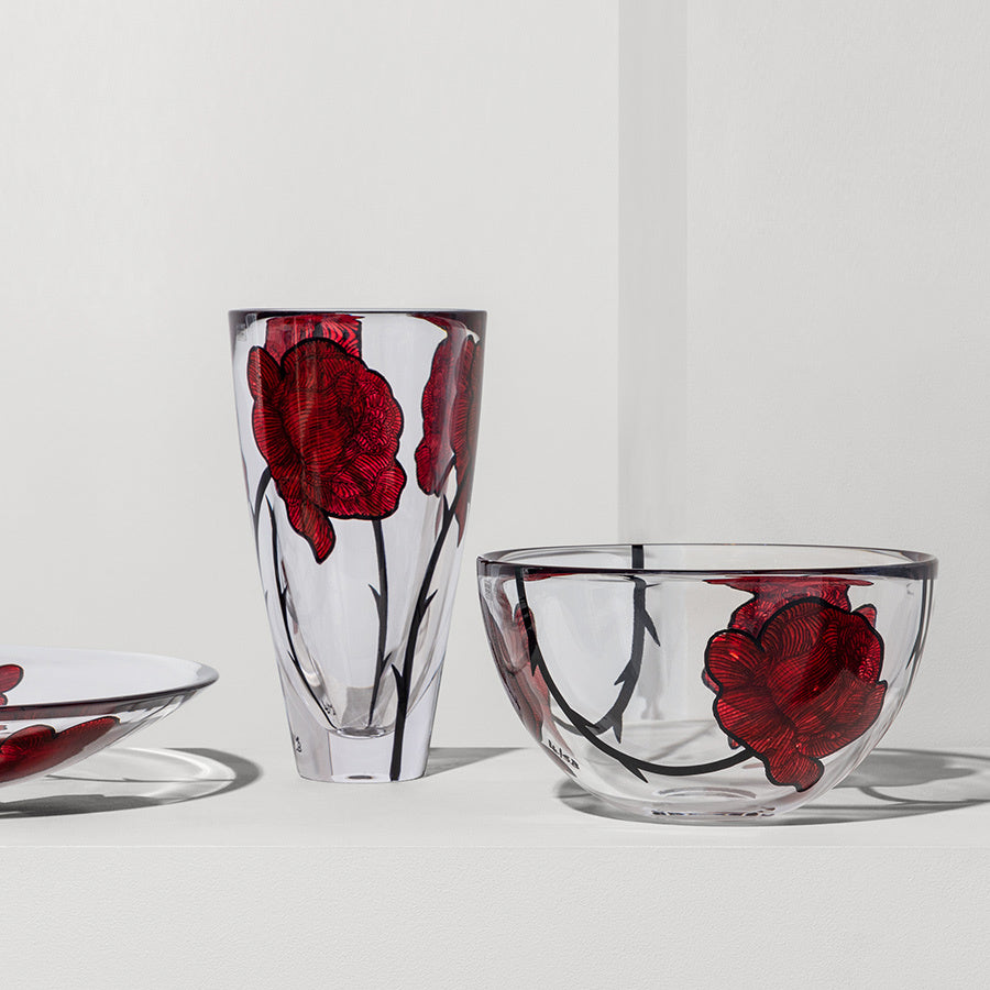 The KostaBoda: Tattoo Vase features exquisite red floral designs on pristine white, accompanied by a hand-painted plate and bowl.