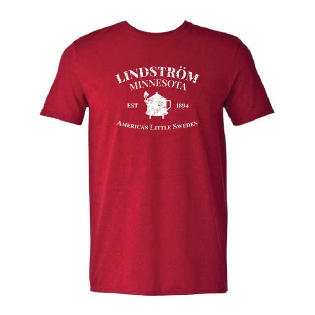 The Tee: Lindstrom Minnesota EST 1894 - Americas Little Sweden is a red tee featuring white Lindström Minnesota Est 1894 text, a Minnesota graphic with a heart, and design elements celebrating the city’s Swedish heritage.