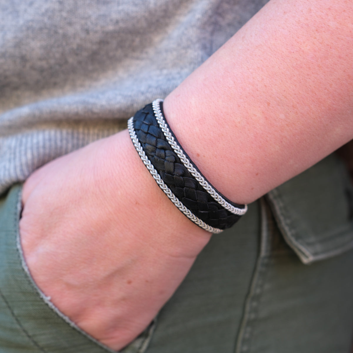 A person wearing the Bracelet: Sami Thor Black 21.5cm with silver accents and a pewter finish slips their hand into the pocket of green pants.