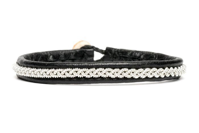 The Sami Tyra Black 16.5cm bracelet is designed with naturally tanned reindeer leather, featuring a silver braided pattern and a single button clasp.