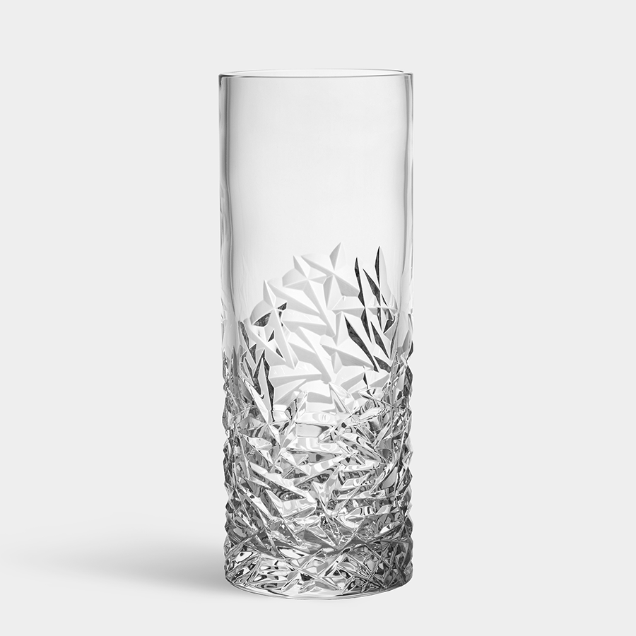 The Orrefors: Carat Vase Lower Cut is a tall, cylindrical glass piece with intricate, textured geometric patterns on the lower half set against a clear background.