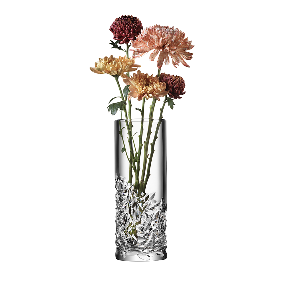 The elegant Orrefors Carat Vase Lower Cut by Lena Bergström beautifully showcases five chrysanthemums in shades of pink and yellow, enhancing their vibrant tones through its clear, textured glass.