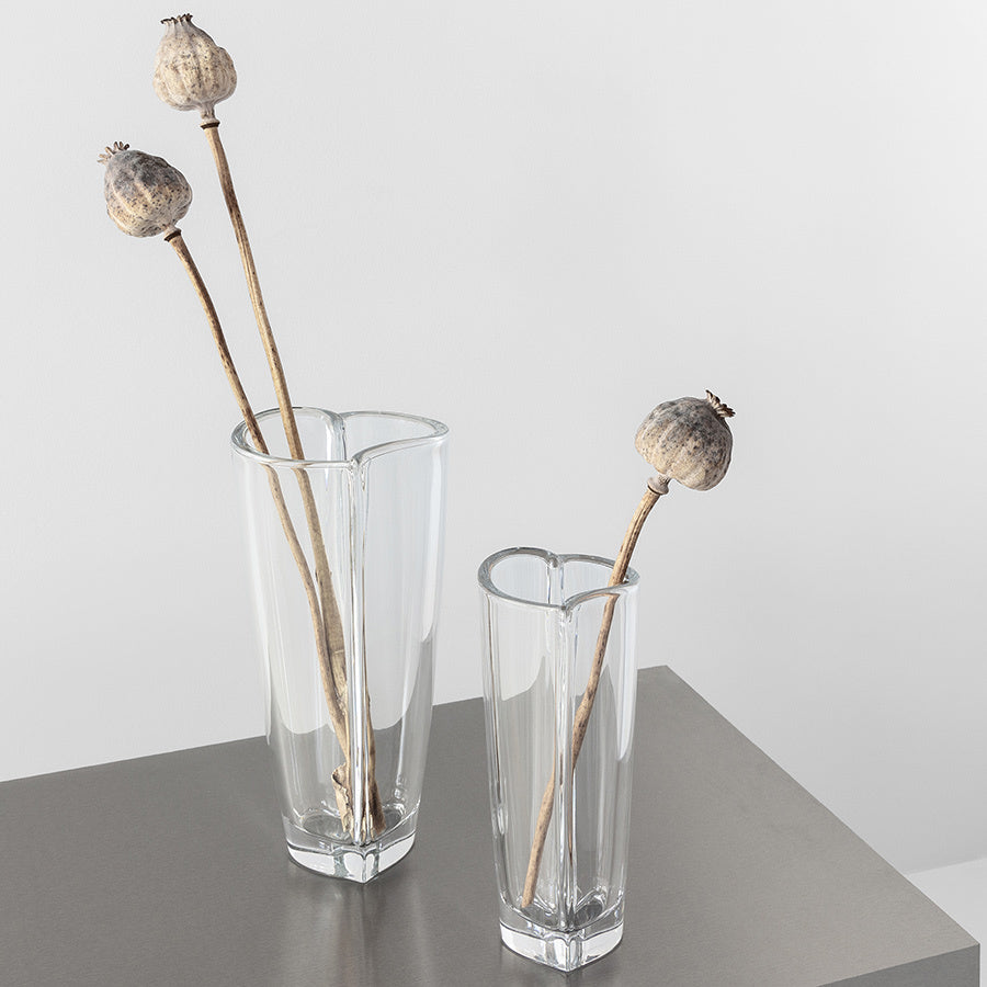 Two Orrefors: Heart Bud Vases Large hold dried poppy stems with round seed pods on a minimalist gray surface against a white background.