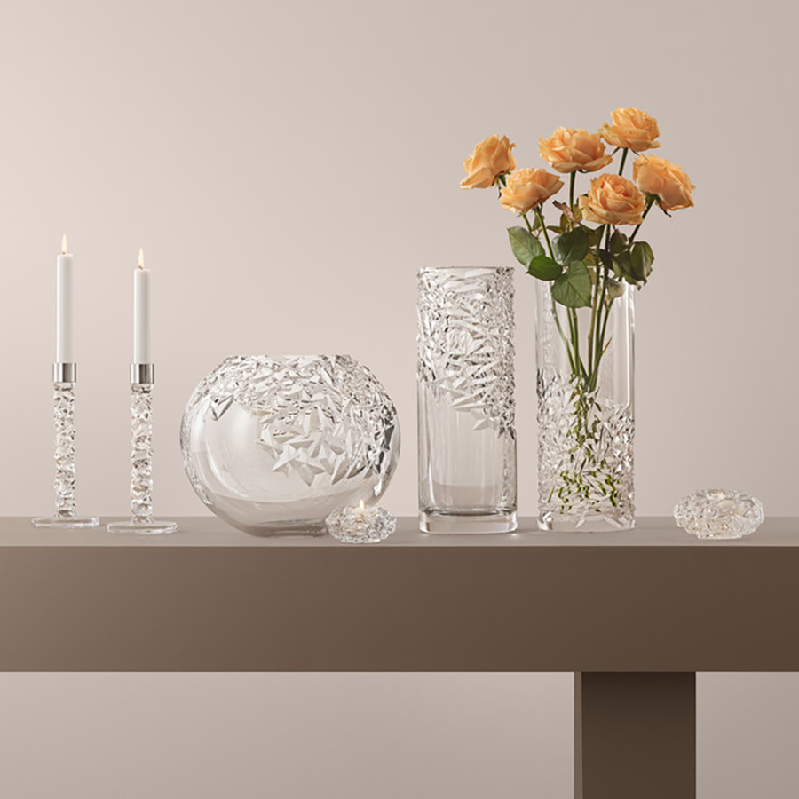 Orrefors Carat Globe Vase XL, holding a bouquet of vibrant orange roses, and crystal glass candle holders with two flickering candles adorn the table.