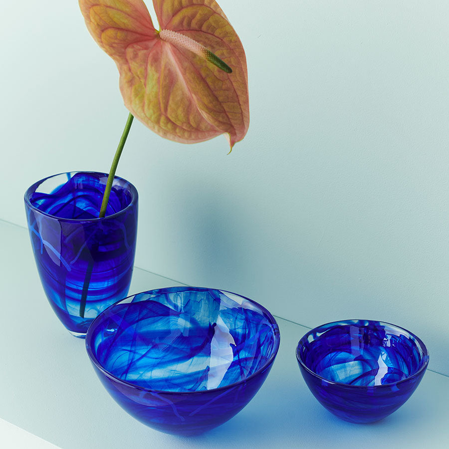 The KostaBoda: Contrast Vase Blue, featuring a pink anthurium by Anna Ehrner, is elegantly arranged with a medium blue glass bowl and a small one on a light surface.