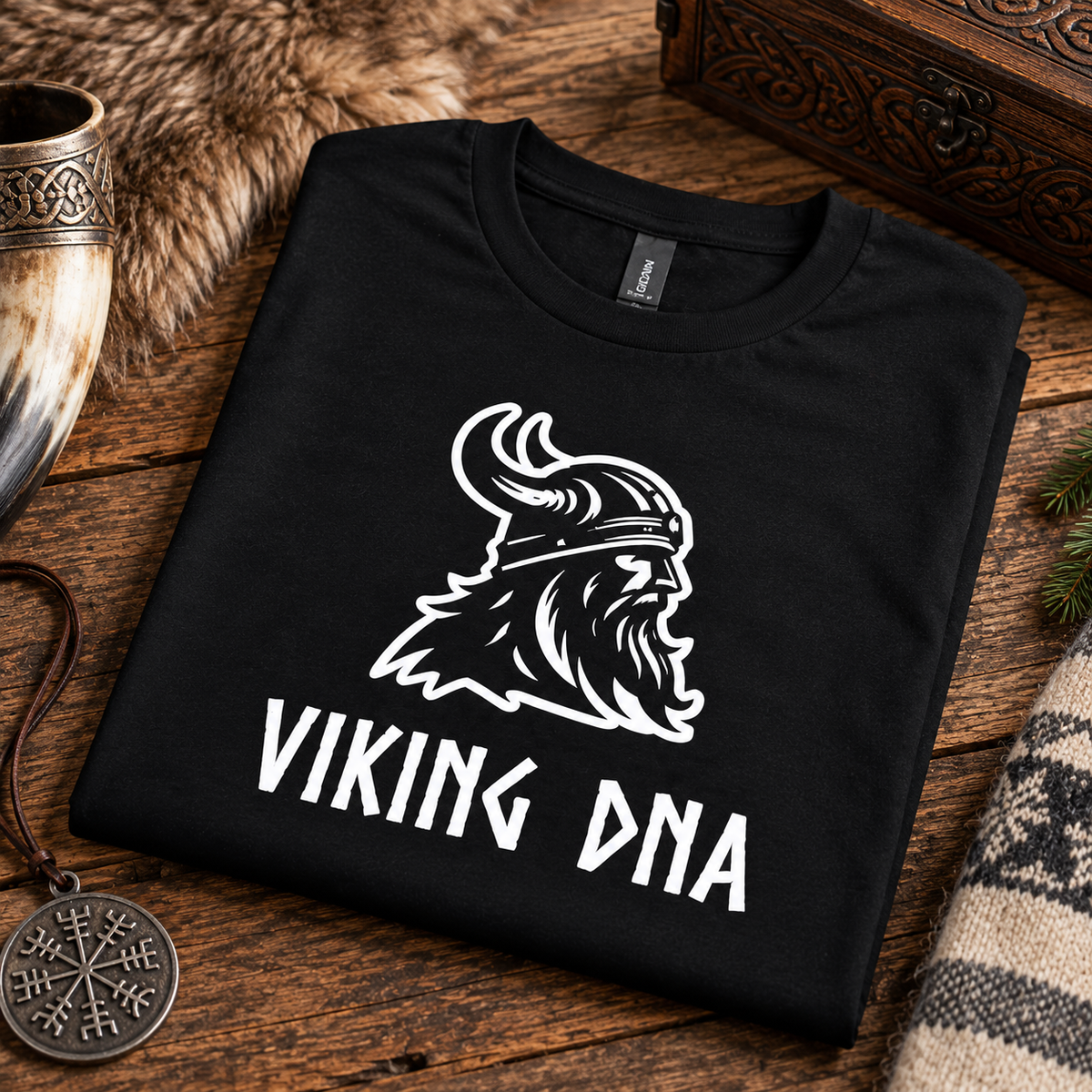 Black shirt folded on wood, displaying a white Viking helmet and “VIKING DNA” text. Nordic-themed items visible around the shirt.