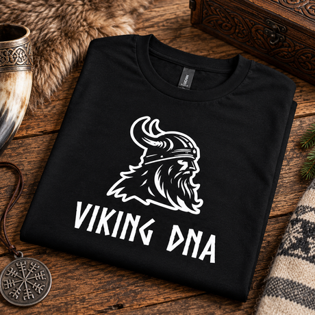 Black shirt folded on wood, displaying a white Viking helmet and “VIKING DNA” text. Nordic-themed items visible around the shirt.