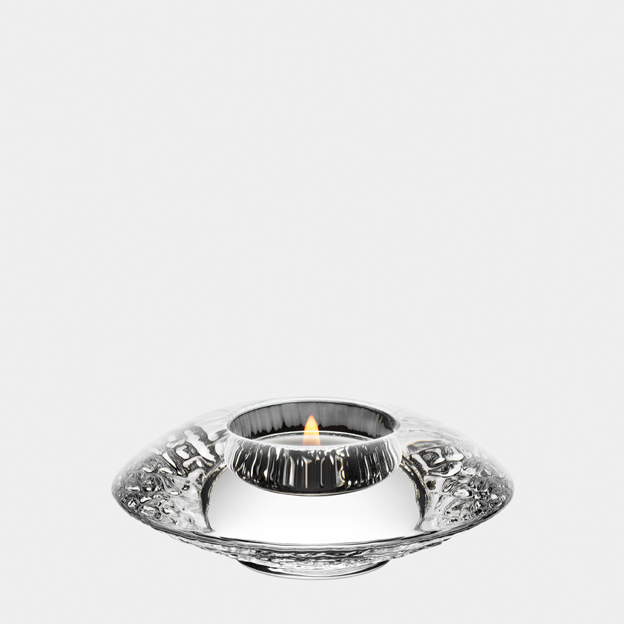 The Orrefors Discus Clear Votive Small Candle Holder, designed by Lars Hellsten, casts a warm glow with its round reflective holder and textured design against a pristine white background.