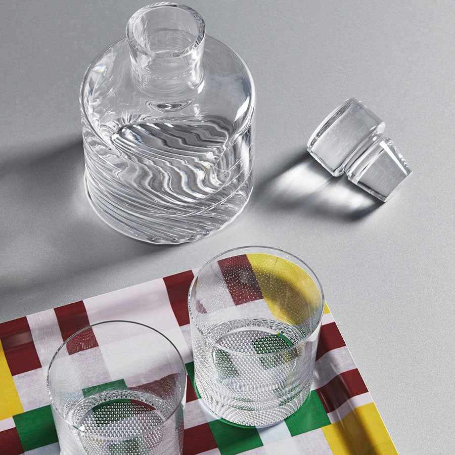 Discover elegance with the KostaBoda Wave 3-Piece Gift Set, including a clear glass decanter, two matching glasses, and a multicolored checkered tray. The bottle cap rests beside them, highlighting Kosta Bodas timeless craftsmanship.