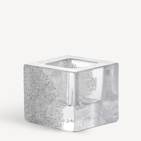 The KostaBoda: Brick Votive Candle Holder, available in 3 colors, features a clear glass cube with a hollow center and textured bubbles inside, elegantly displayed on a plain white background.