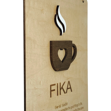 Wooden plaque featuring a heart-shaped coffee cup cutout with rising steam and the word “FIKA” below, displayed on a light wood background.