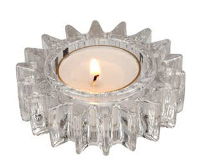 A lit tealight candle rests in the Candle Holder: Glass Wheel Gear Tealight Holder, featuring a transparent design with a jagged edge and a 3 1/8 inch diameter.