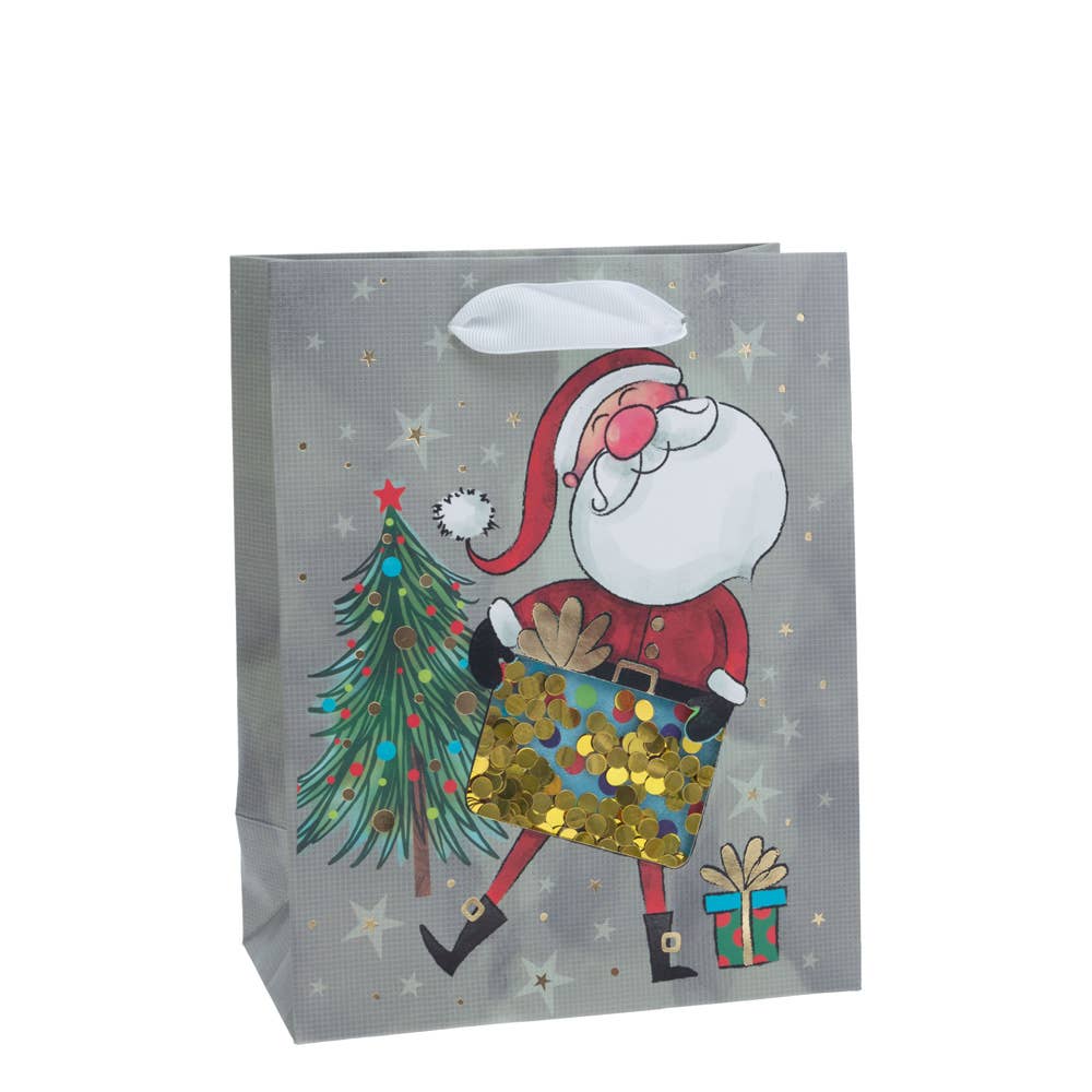 The Gift Bag: Jolly Santa Sequin Medium Gift Bag Christmas features a cheerful Santa Claus holding a ornate present, positioned next to a glimmering Christmas tree and a small wrapped gift with twinkling stars in the backdrop.