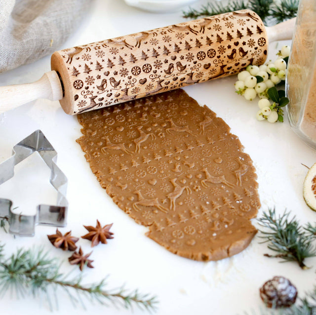 The Rolling Pin: Reindeer Birds & Trees Embossing Rolling Pin, inspired by Scandinavian design and handmade craftsmanship, skillfully embosses gingerbread dough with detailed snowflake and Christmas deer patterns amidst a selection of festive cookie cutters and decorations.