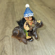 The "Troll: Troll on Moose" figurine captures the whimsical charm of Norway, showcasing a small gnome in a blue hat and colorful pants sitting atop a moose on a wooden surface.