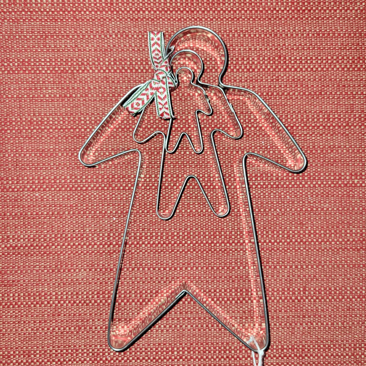 The Cookie Cutter: Ginger Bread Man 3-Set, featuring two gingerbread men-shaped cutters nested together and adorned with a patterned ribbon around the larger one, crafts a delightful display on a textured red surface inspired by traditional Swedish design.