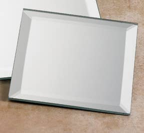 The Candle Holder: Mirror Plate for Ball or Pillar Candles 4" x 4" features beveled edges and sits on a light brown surface, ideal for displaying your favorite pillar or ball candles.