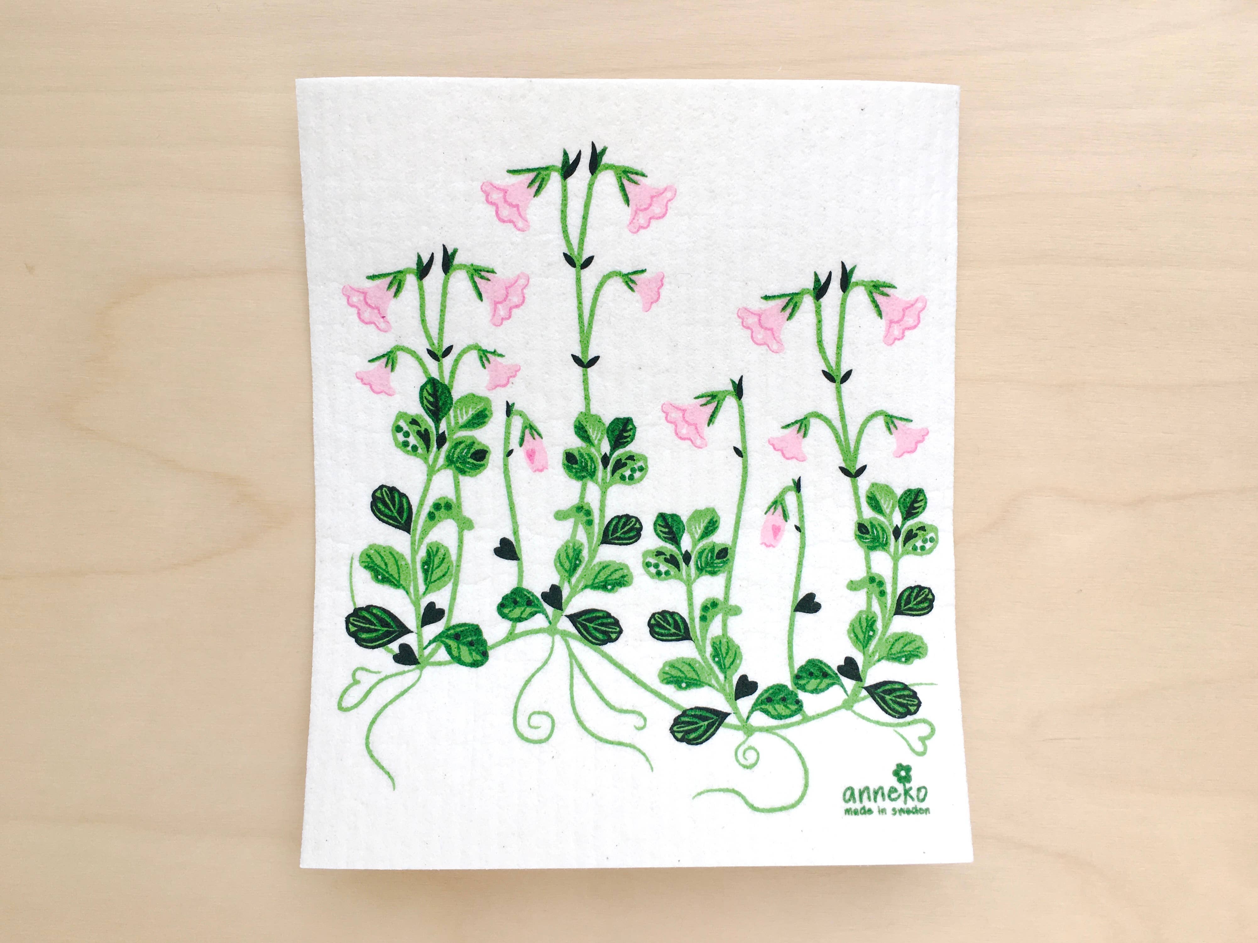 The Linnea Flowers Swedish Dishcloth features a botanical pattern with green vines and pink flowers on a light wooden surface. This eco-friendly, biodegradable dishcloth is highly absorbent, combining sustainability with style for an eco-conscious kitchen choice.