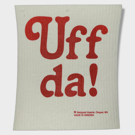The "Dish Cloth: Uff da!" features vibrant red text on a white background, highlighting "Uff da!" in bold letters. At the bottom, it notes its creation in Sweden by Bergquist Imports, Cloquet, MN. This super absorbent and eco-friendly dish cloth is ideal for effortlessly handling kitchen messes.