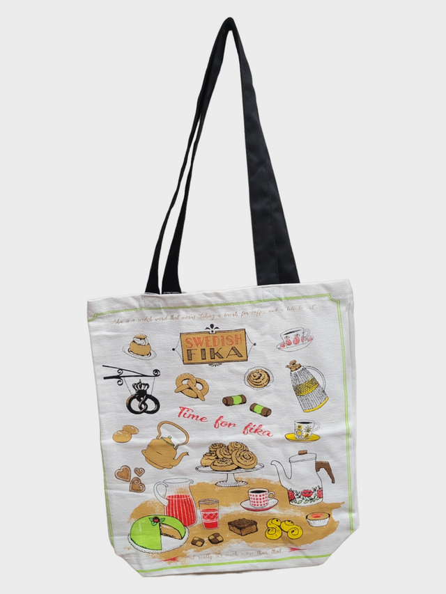 Introducing the Tote: Fika Shopping Tote, a textile bag adorned with whimsical cartoon designs of Swedish fika essentials such as coffee pots, pastries, and cups. The tote features the phrases "Swedish Fika" and "Time for Fika," set against a white background and complemented by black handles.