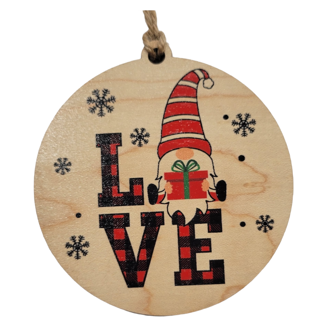 Introducing the Ornament: Love Gnome - Wood, a round wooden piece that showcases a gnome holding a gift in place of the 'O' in 'LOVE', encircled by delicate snowflakes—ideal for adding charm to your Christmas decor.