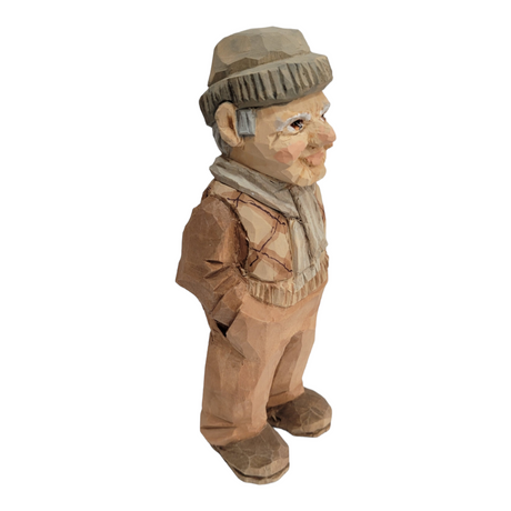 This 6 1/2 inch "Milo" wood carved figure by Bill Erickson portrays an elderly man clad in a cozy hat and scarf, standing with his hands in his pockets.